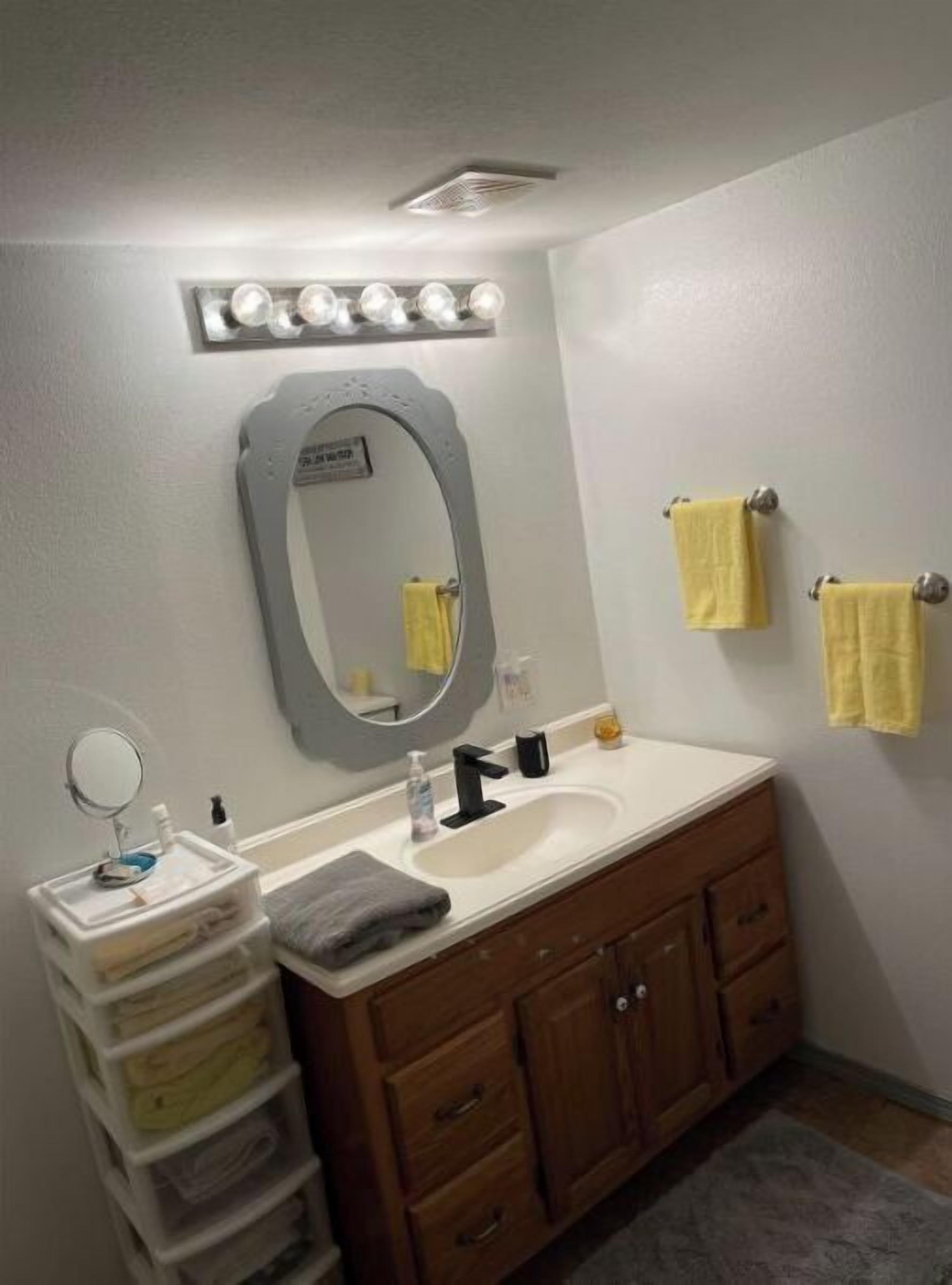 A bathroom with a vanity, a sink, a mirror, and a towel rack.