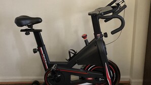 Una bicicleta estática en una habitación con un espejo en la pared y un televisor a la derecha.