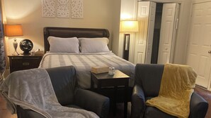 Habitación de hotel con cama, dos sillones, una mesita de noche, lámpara y un panel decorativo en la pared.