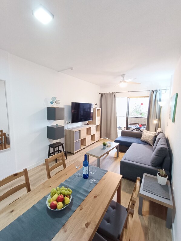A modern living room with a dining area, a flat-screen TV, and a sofa.