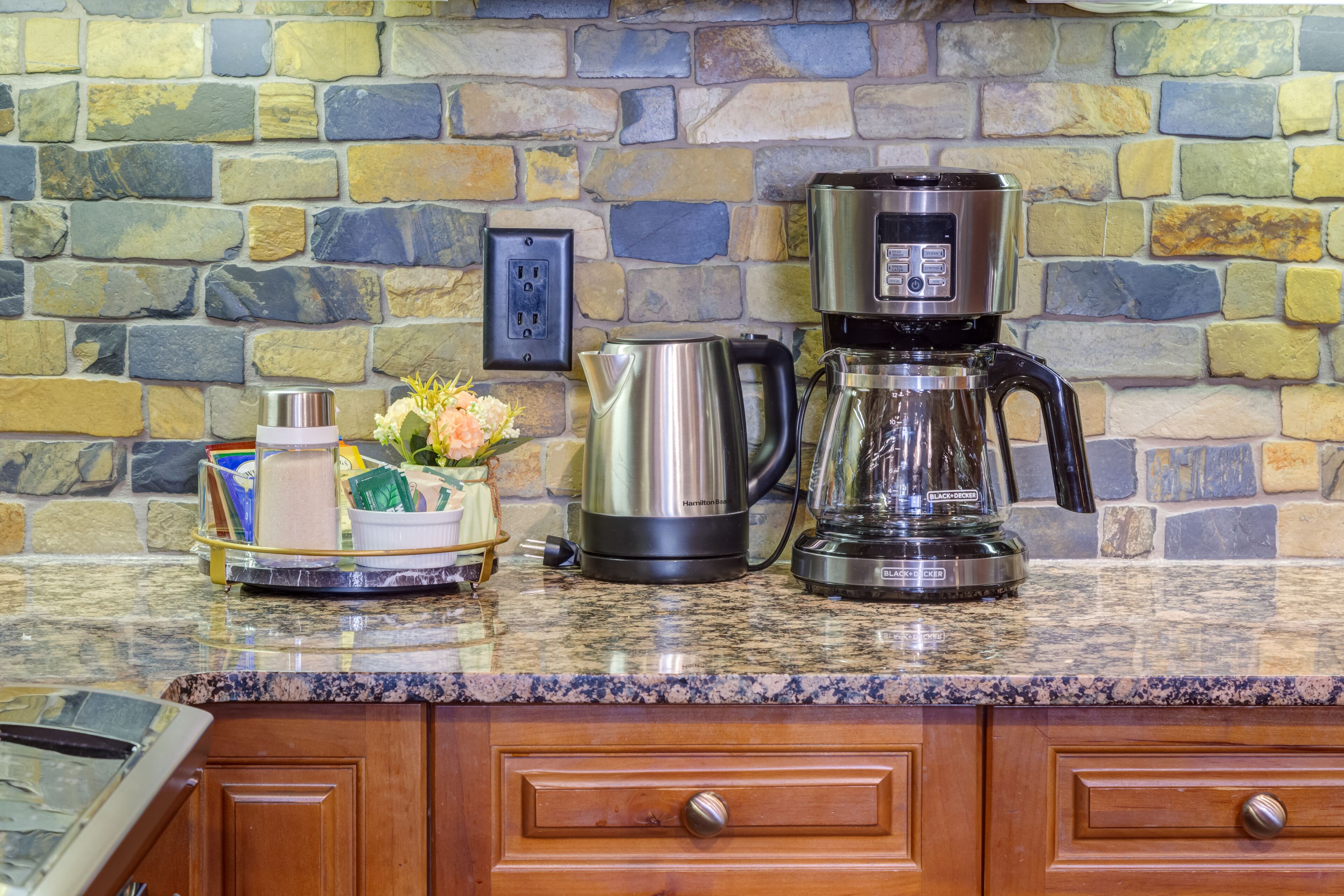 Una cocina con encimera de granito, cafetera, hervidor y salpicadero de piedra.