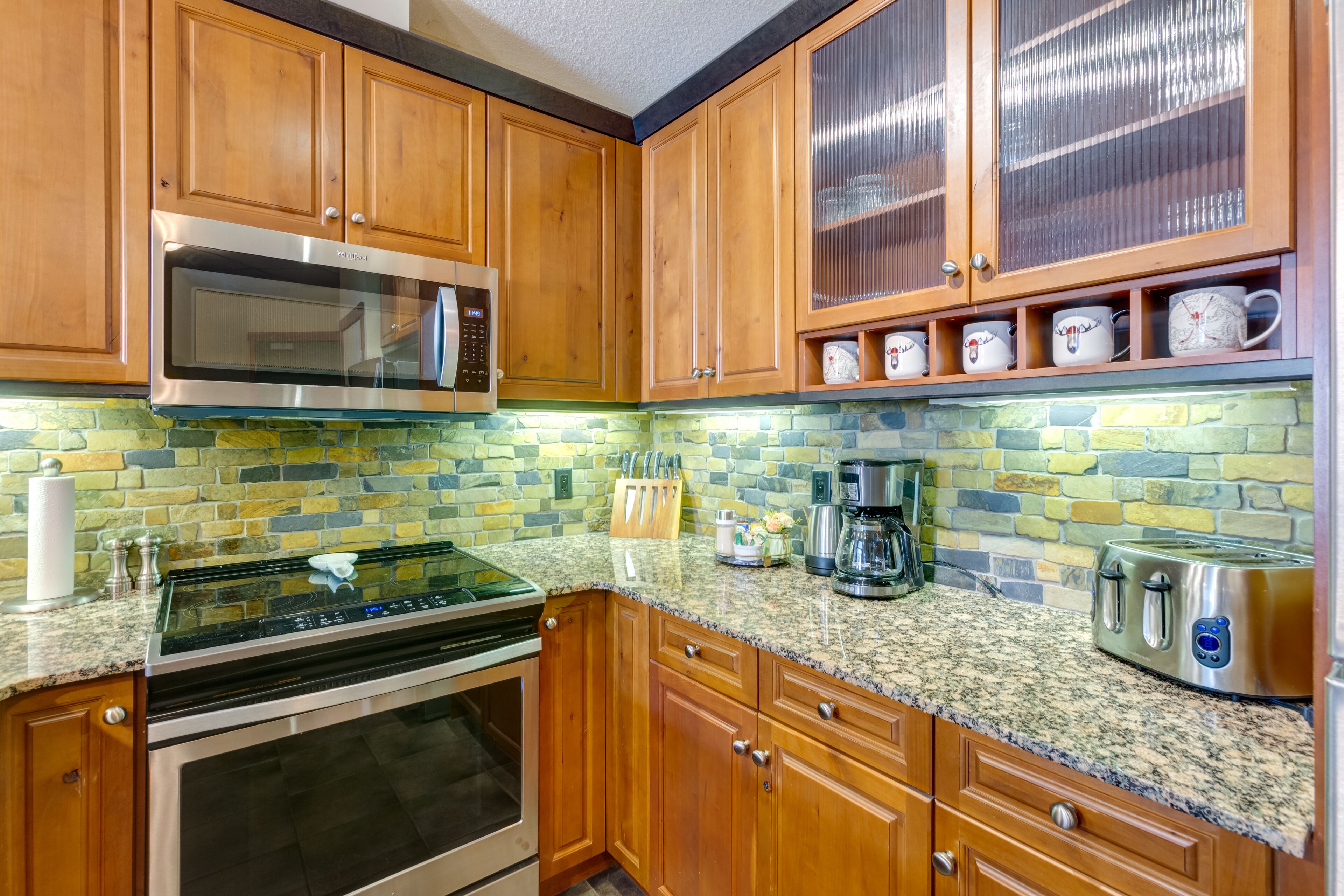 A kitchen with wooden cabinets, a stainless steel microwave, a stove, a coffee maker, and a toaster.