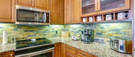 A kitchen with wooden cabinets, a stainless steel microwave, a stove, a coffee maker, and a toaster.