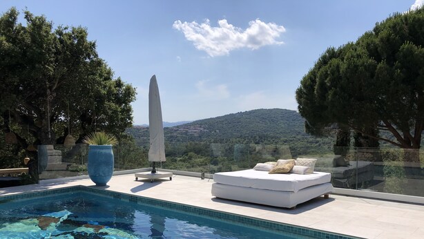 A pool with clear water, a white sofa, and a view of a mountainous landscape.