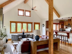 A spacious living area with a high ceiling, wooden beams, and large windows offering a view of the outdoors. - Spectacular Private Big Sky 5 Bedroom Home - BEST LOCATION ! (Big Sky)