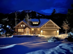 A two-story house with a garage, surrounded by snow-covered landscape and mountains in the background. - Spectacular Private Big Sky 5 Bedroom Home - BEST LOCATION ! (Big Sky)