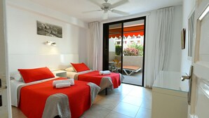 A hotel room with two beds, a ceiling fan, a balcony with a table and chairs, and a view of the outside. - A. Parque Santiago 1-1 bed-pool-sea front location. Sunny. (Playa de la Américas)