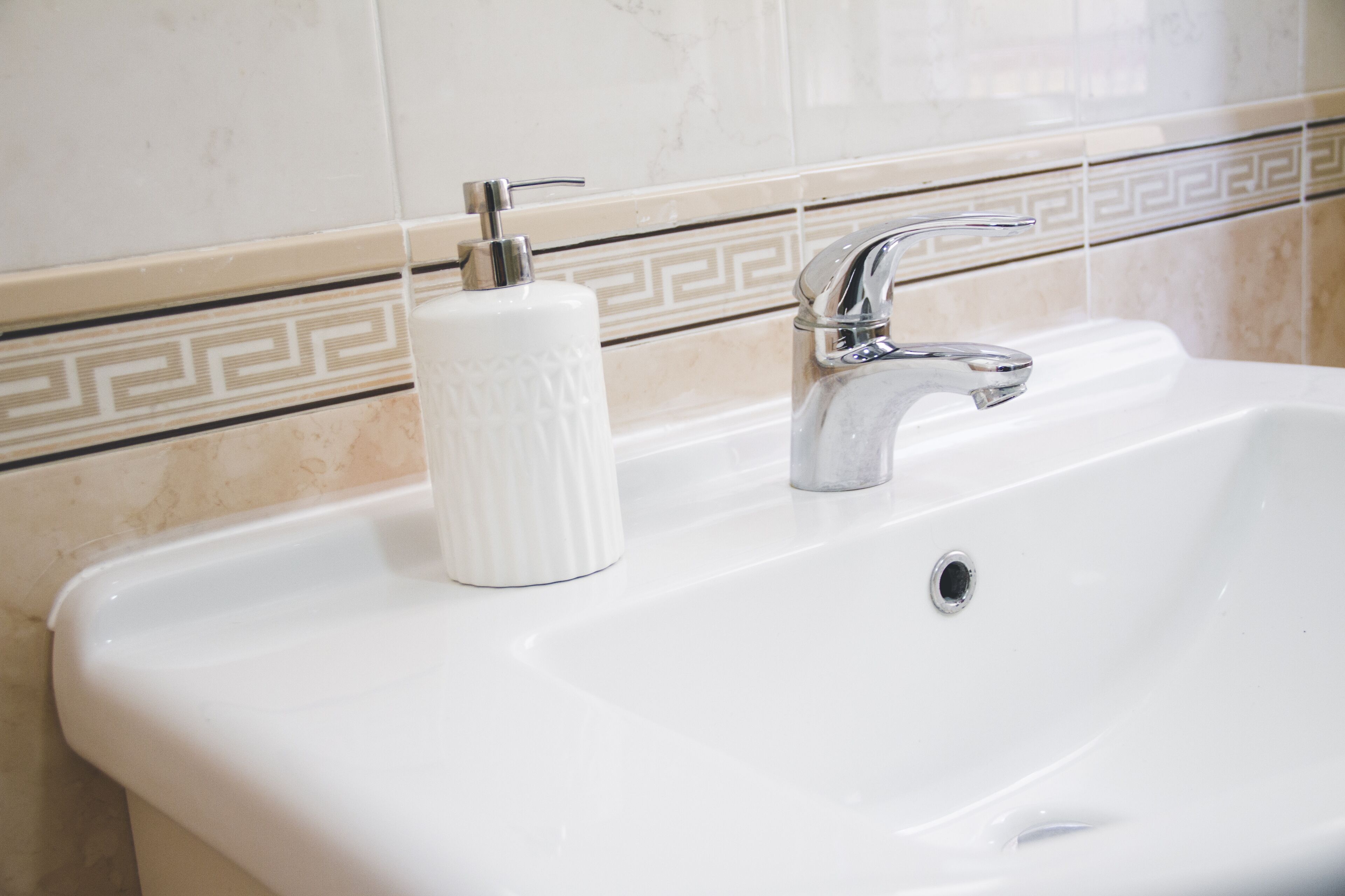 A white bathroom sink with a chrome faucet and a soap dispenser.