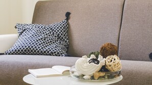 A modern living room with a grey sofa, a patterned pillow, a small round table with a book and decorative items. - Palazzo dei Lari (Scafati)