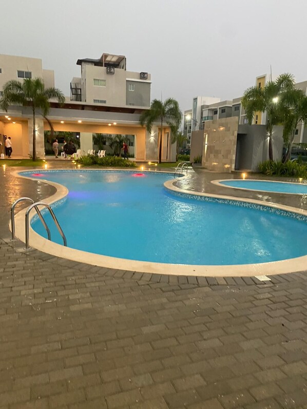 Una piscina de borde curvo, rodeada por un camino pavimentado y palmeras.