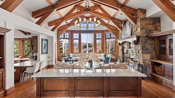 A spacious kitchen with a large island, wooden beams, stone fireplace, and large windows. - 5 Bed/ 5.5 Bath Ski-In, Ski-Out  Home in Exclusive Two Creeks Neighborhood (Snowmass Village)