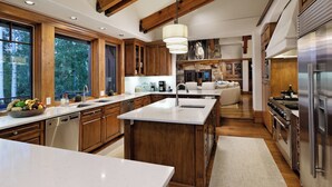 A modern kitchen with wooden cabinets, a large island, stainless steel appliances, and a stone fireplace. - 5 Bed/ 5.5 Bath Ski-In, Ski-Out  Home in Exclusive Two Creeks Neighborhood (Snowmass Village)