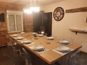 A dining area with a long wooden table set for six, clear chairs, and a wall clock. - Cocooning in the valley of the lakes (Xonrupt-Longemer)