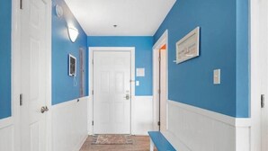 Een hal met blauwe wanden, witte deuren en een bankje.