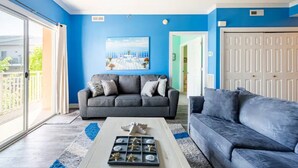 Een woonkamer met een grijze bank, een blauwe accentmuur en een groot raam.