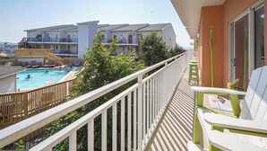 Een balkon met een zwembad, witte stoelen en uitzicht op een gebouw met meerdere balkons.