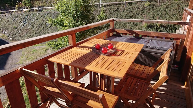 A wooden deck with a table and chairs, a tray with red cups, and a view of a hillside.