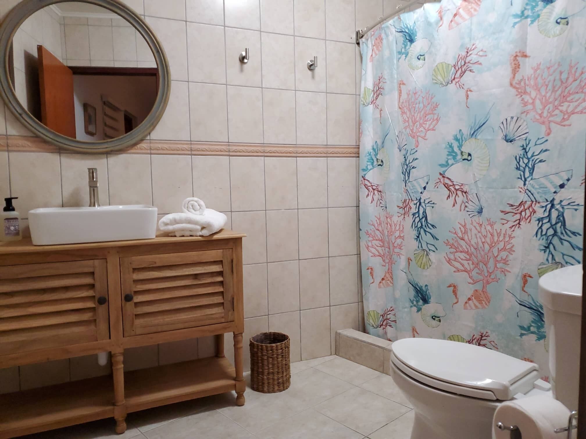 A bathroom with a wooden vanity, a sink, a toilet, and a shower curtain with a coral pattern.