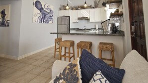 Un saló modern amb zona de cuina, amb un sostre alt amb bigues a la vista, zona de menjador amb tamborets i un conjunt d'aixetes acollidor amb una manta estampada.
