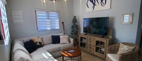 Un salon moderne avec un canapé d’angle, une table basse, un téléviseur et un sapin de Noël.