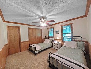Un dormitorio con dos camas individuales, un ventilador de techo, una mesita de noche con lámpara y una ventana con persianas.