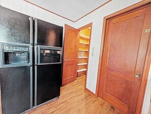 Eine Küche mit einem schwarzen Kühlschrank, Holzschränken und einer Holztür, die zu einem Vorratsraum führt.