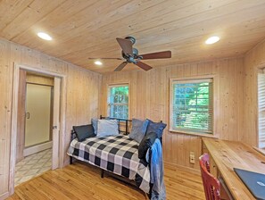 A wooden-paneled room with a bed, a ceiling fan, a window with blinds, and a door. - Pet Friendly 4 Bedroom River Overlook on 7 Acres (Newland)
