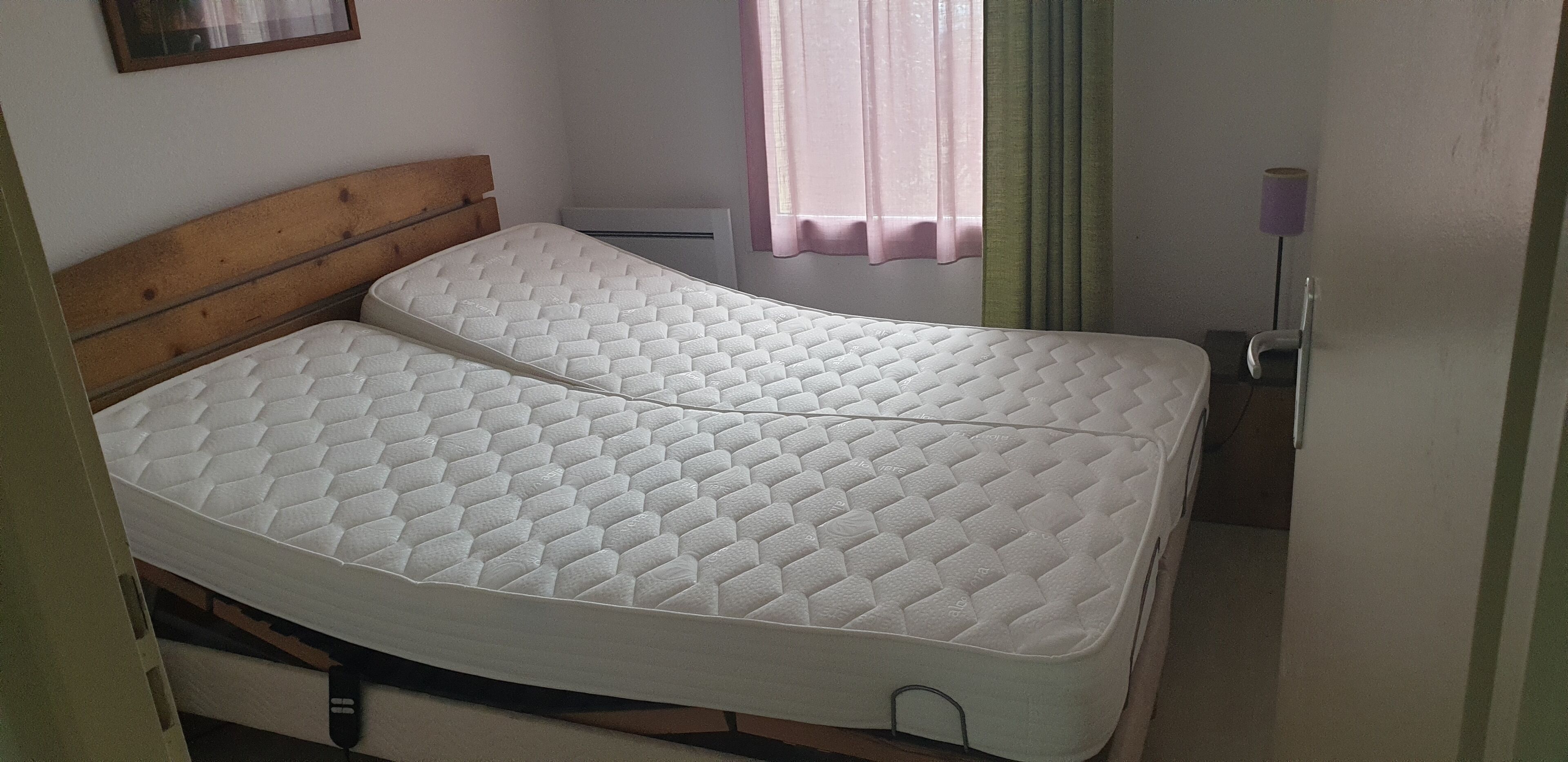 Een enkel bed met een houten hoofdeinde in een kamer met een raam, een wandairconditioner en een lamp.