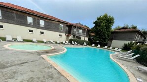 En swimmingpool med to afdelinger, omgivet af liggestole og en bygning med et tagdækket tag.
