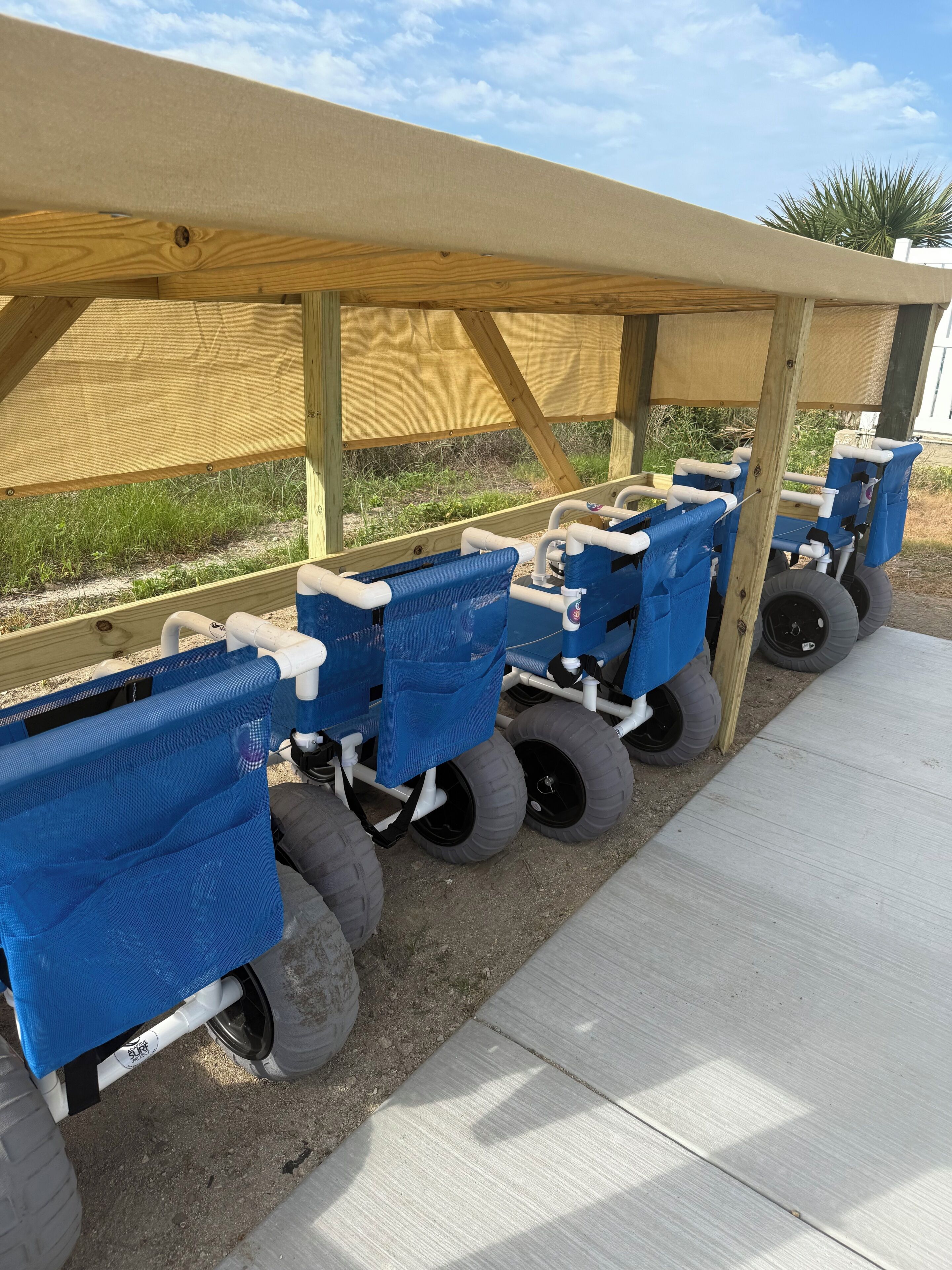 A row of blue carts with wheels, under a wooden structure with a beige canopy.