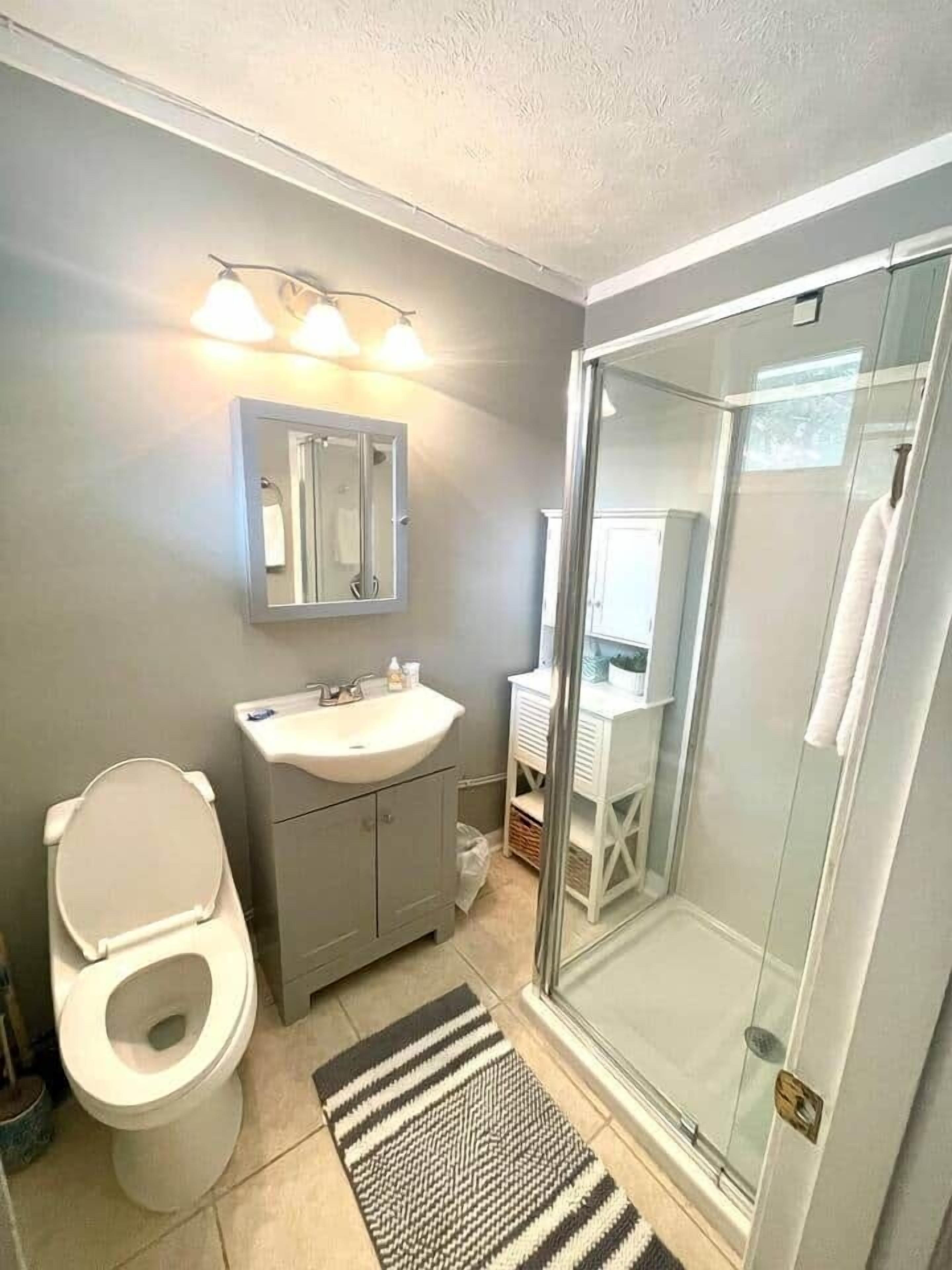 A bathroom with a toilet, sink, mirror, and glass shower enclosure.