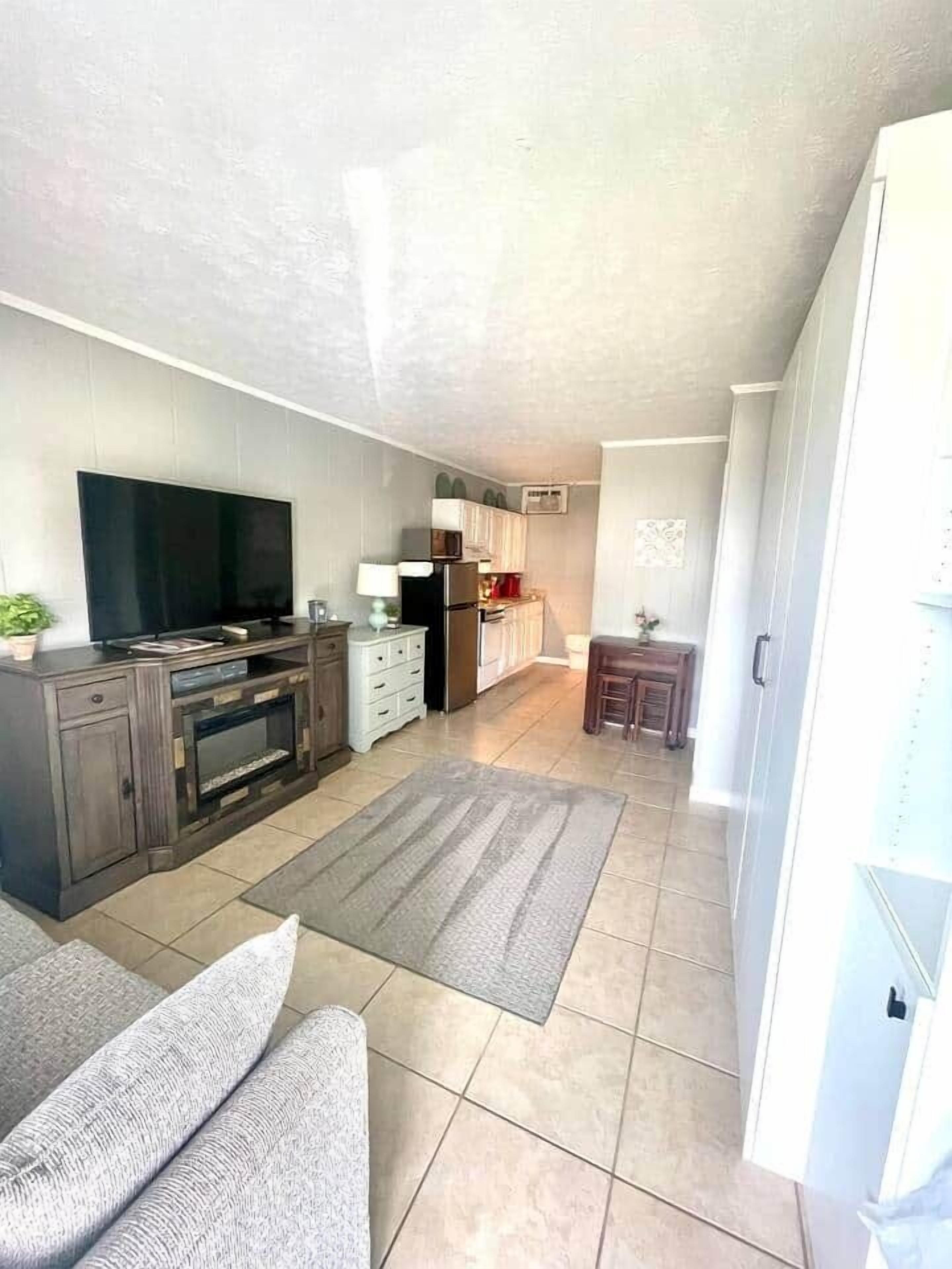 A compact living space with a flat-screen TV, a kitchen area with a refrigerator, and a dining area with a small table and chairs.