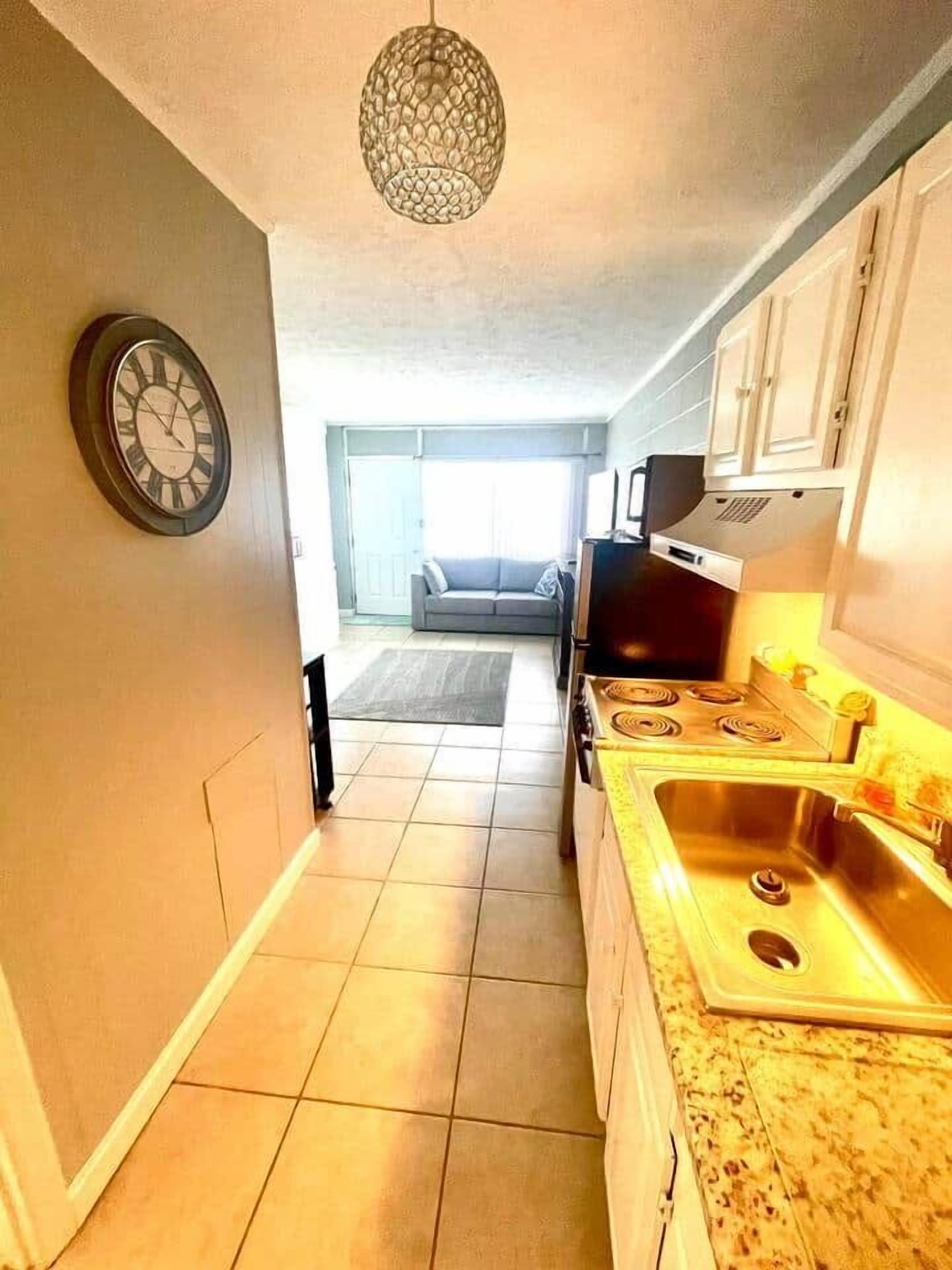 Une petite cuisine étroite avec une horloge, une cuisinière et un évier.