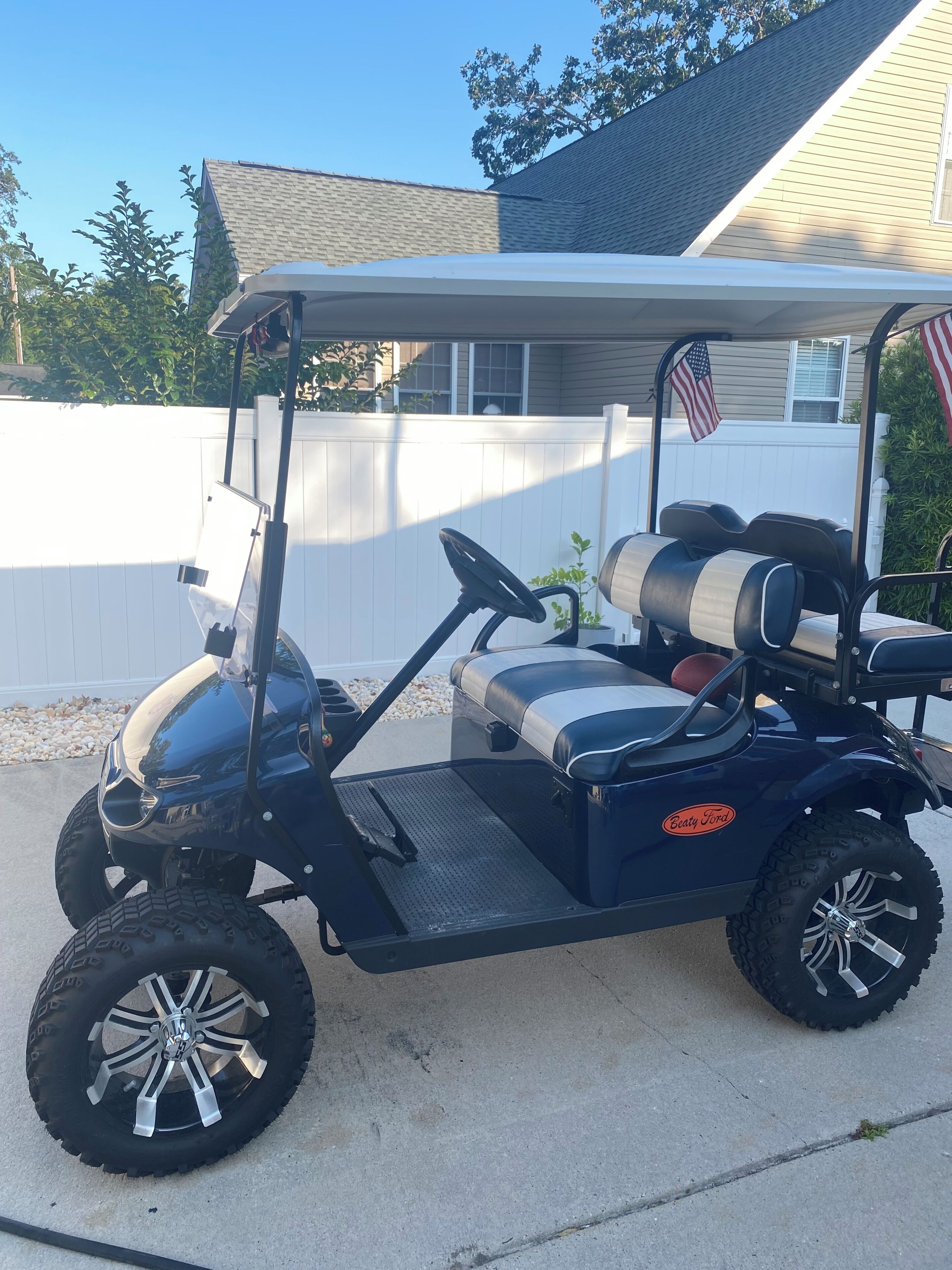 A golf cart parked on a driveway with a white fence and a house in the background.