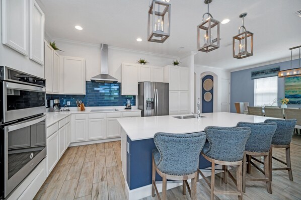 A modern kitchen with white cabinets, a large island, stainless steel appliances, and blue accent walls. - Stylish Family Villa With Private Pool and Hot Tub (Reunion)