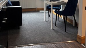 Ein modernes Wohnzimmer mit einer Couch, einem Esstisch, Stühlen, einem Fernseher und einem Fenster mit Jalousien.