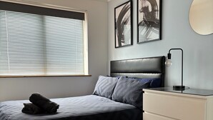 Ein Schlafzimmer mit einem Bett, einem Nachttisch mit Lampe, einer Kommode und zwei gerahmten Bildern an der Wand.