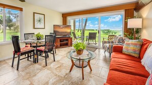 A living room with a glass table, a sofa, and a TV. There are chairs and a plant. - Ocean Front, Ground Level 1 Bedroom with King, Sleeps 4, with Cold AC (Kapaʻa)