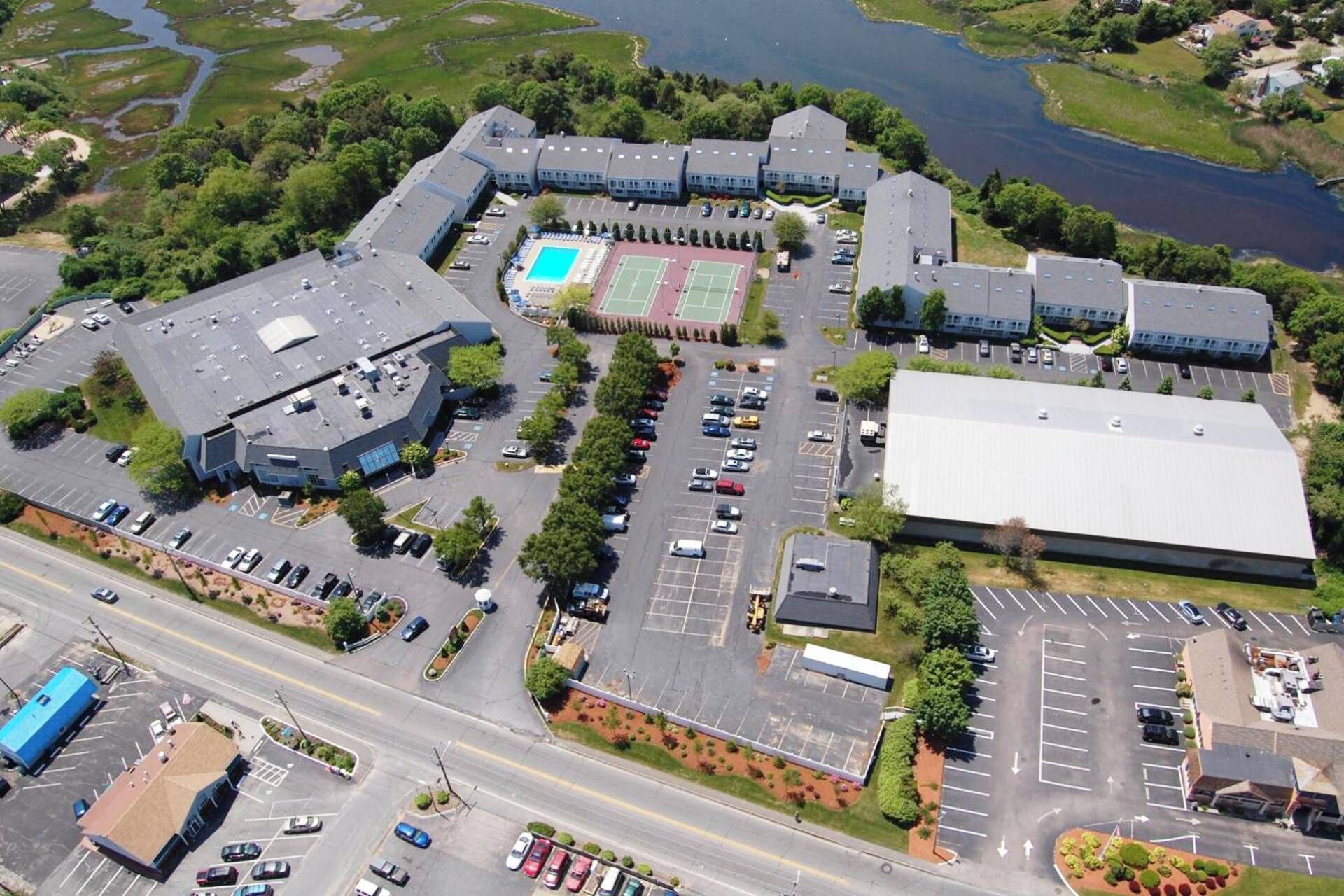 An aerial view of a commercial building complex with multiple parking lots, a tennis court, and a large building with a flat roof.