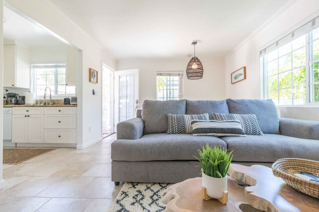 A modern living room with a grey sofa, a coffee table with a plant, and a kitchen in the background.