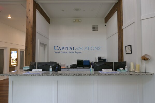 A reception desk with a sign reading 'CAPITALVACATIONS' and a slogan 'Travel. Gather. Smile. Repeat.'