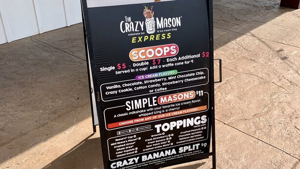 A black signboard for 'The Crazy Mason' milkshake bar and ice cream shop with menu options and prices.
