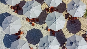 Una playa con múltiples sombrillas blancas y sillas de madera dispuestas en un orden.