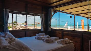 Quarto com cama, vista para a praia e teto de madeira.