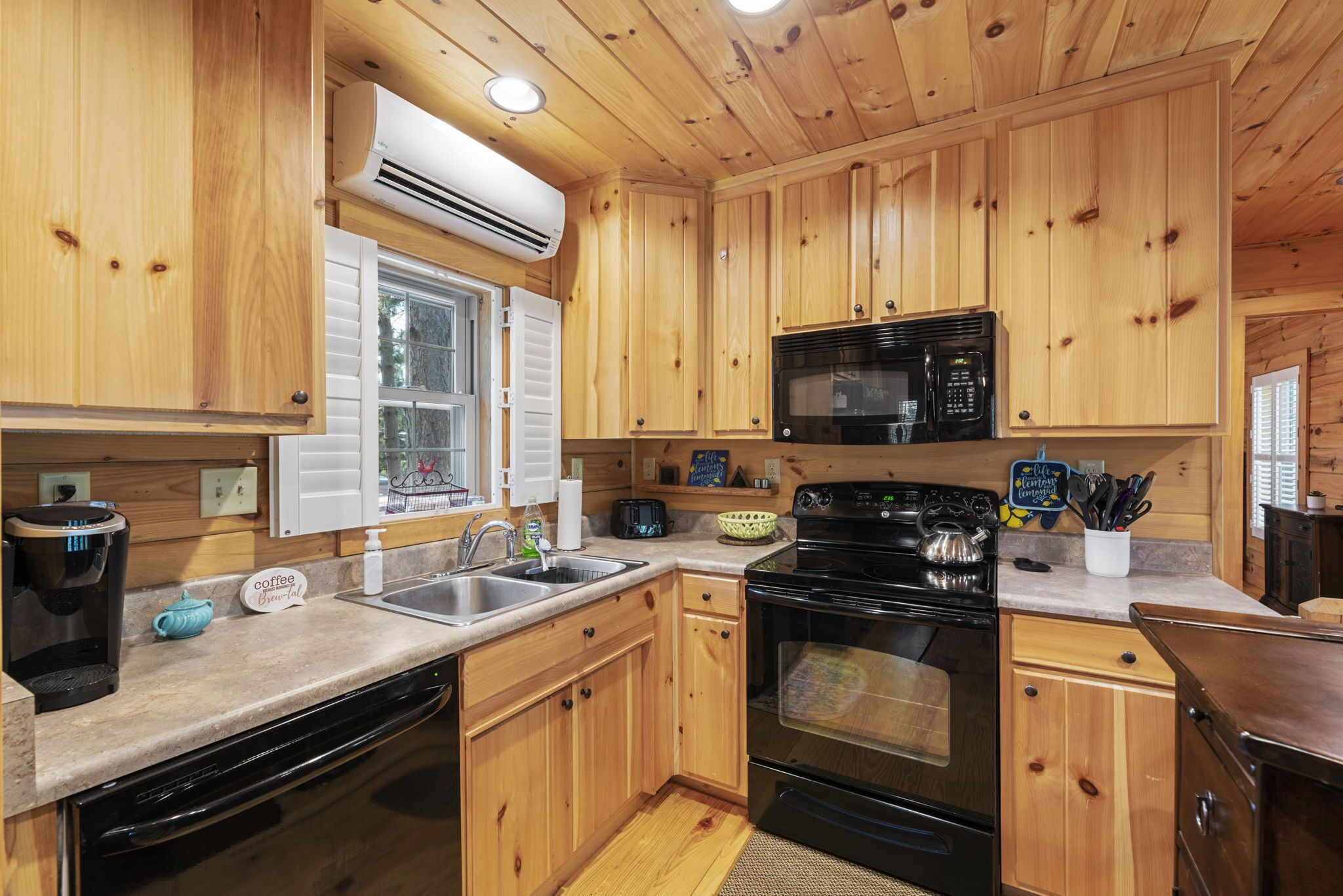 A wooden cabin kitchen with a dishwasher, stove, microwave, and a coffee station.