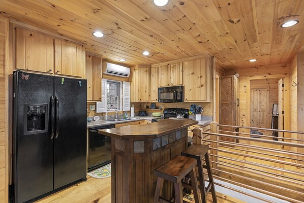 A wooden cabin-style kitchen with a central island, a refrigerator, a microwave, and bar stools.