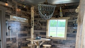 A rustic interior with a wooden table and stools, a window with a view, and a sign that reads "Life is better on the patio." - Secluded Cabin w/ Private Pond/ Peaceful Getaway (Cameron Mills)