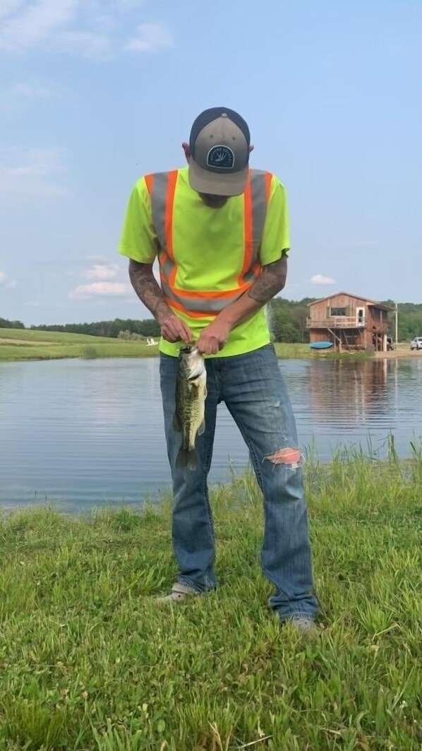 A person holding a fish by a lake with a house in the background. - Secluded Cabin w/ Private Pond/ Peaceful Getaway (Cameron Mills)