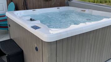 A hot tub with a wooden exterior, a control panel, and a step leading into it.