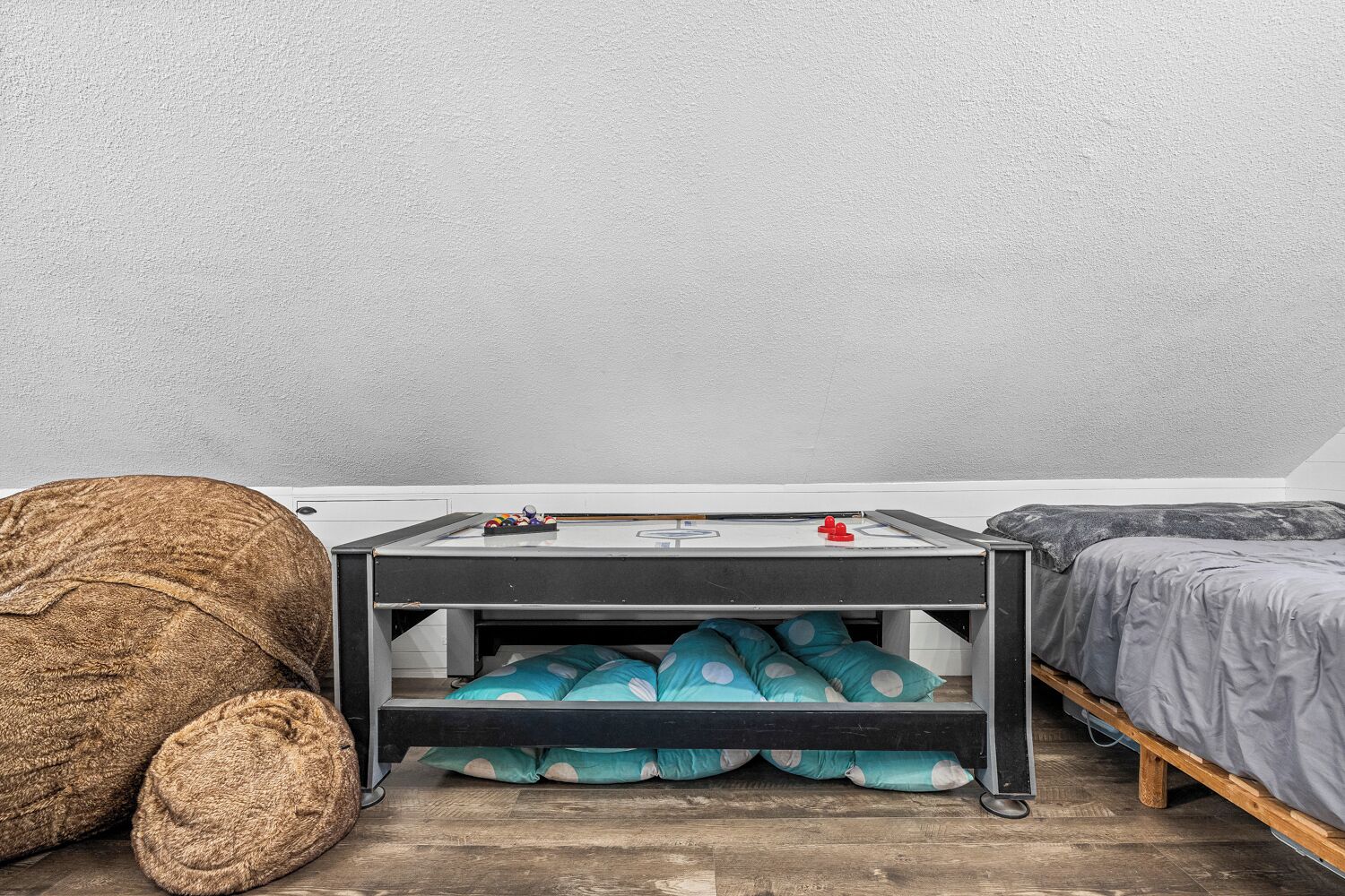 Une pièce de taille modeste comprenant un lit, une petite table avec un billard, et un fauteuil en forme de sac.